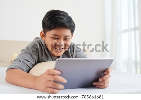 Asian boy lying on the floor in his room and a reading book on digital tablet