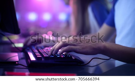 Close-up On Gamer's Hands on a keyboard, Actively Pushing Buttons, Playing MMO Games Online. Background is Lit with Neon Lights. Royalty-Free Stock Photo #705666394