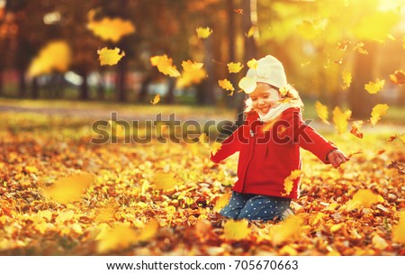 happy child girl throws autumn leaves and laughs outdoors
