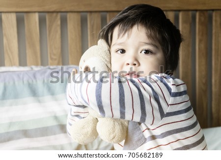 Cute toddler boy siting in bed with his pyjamas and cuddle his teddy bear, Kid wake up in the morning in his bedroom in retro tone