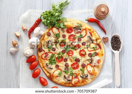 Fresh homemade pizza with tomatoes, salami, cheese and mushrooms with food ingredients and spices for cooking  on piece of baking paper. Top view
