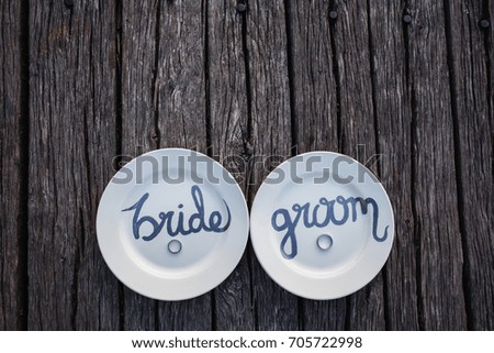 Wedding concept. Wedding rings on plate with inscription Bride and Groom on vintage wooden background with copy, empty space.