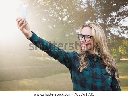 Digital composite of Millennial woman taking selfie in blurry park with flare