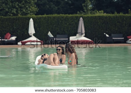 Young ladies sit in the pool and enjoy the summer and the excellent sun while tanning on the floating sunbed.Dream the perfect holiday in a seaside resort sunbathing in the middle of nature having fun