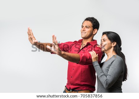 stock photo of Indian smart and cheerful / happy couple indoor, husband composing frame in the newly purchased or rented house and wife accompanying, indian couple and real estate concept