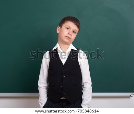 indifferent school boy portrait near green blank chalkboard background, dressed in classic suit, one pupil, education concept