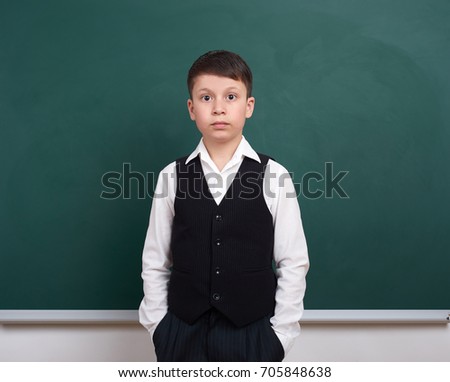 indifferent school boy portrait near green blank chalkboard background, dressed in classic suit, one pupil, education concept