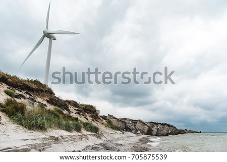 Wind turbine next to the sea on a  blue cloudy sky background.