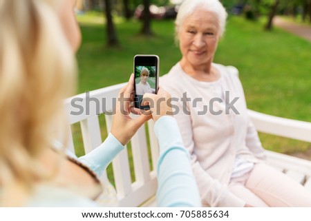 family, technology and people concept - young daughter with smartphone photographing her happy smiling senior mother at park