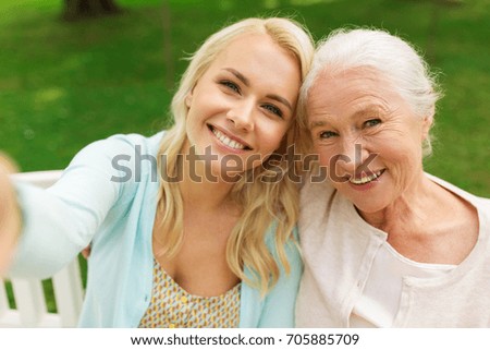 family, technology and people concept - happy smiling young daughter and senior mother sitting on park bench and taking selfie