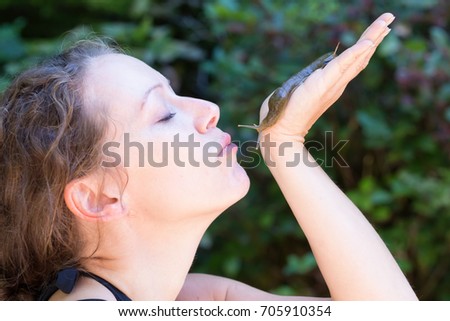 Beautiful middle age Caucasian woman is holding a slug in her hand and forming her lips for a kiss. Picture taken in Tofino, Vancouver Island, British Columbia, Canada.