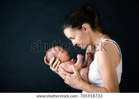 Young mother, kissing and hugging her newborn baby boy, tender, care, love, positive emotions. Isolated image, black background