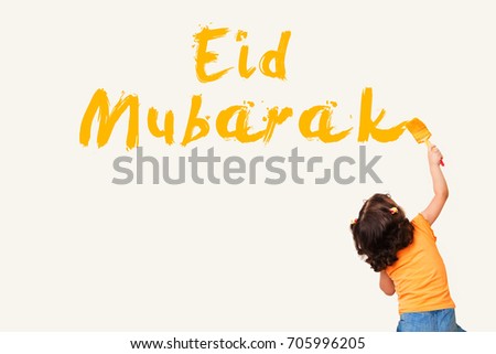 Greeting Card : Eid Mubarak - Arabic Translation : Blessed Feast - Muslim girl painting Eid Mubarak on the wall using paint brush Royalty-Free Stock Photo #705996205