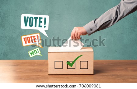 A hand placing a voting slip into a ballot box Royalty-Free Stock Photo #706009081
