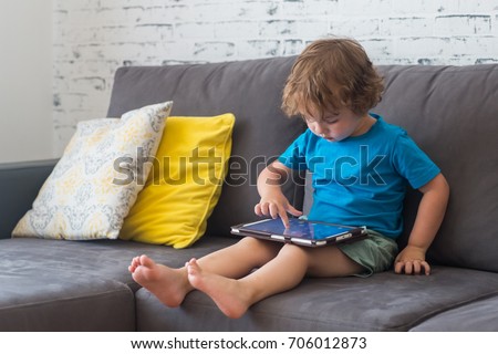 Little cute boy in a blue T-shirt playing games on a tablet and watching cartoons