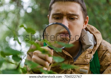 Portrait of young botanist with magnifying glass in forest on summer day