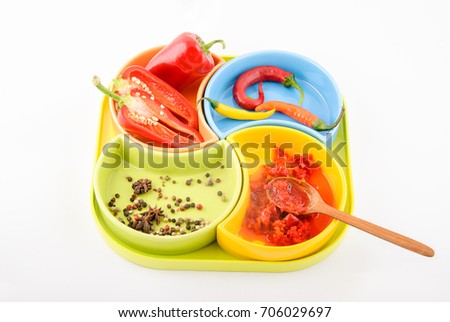 Seasoned sauce with paprika and red hot chili peppers on multi-colored plates, on white