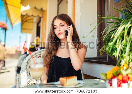 Lifestyle modern portrait of young stylish hipster woman at cafe on the street and talking on the mobile phone and drinking hot latte,eatting cheesecake slice and smiling enjoy weekends.
