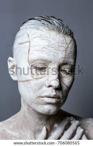 Art portrait of woman covered in clay isolated over grey background. Woman face like cracked earth