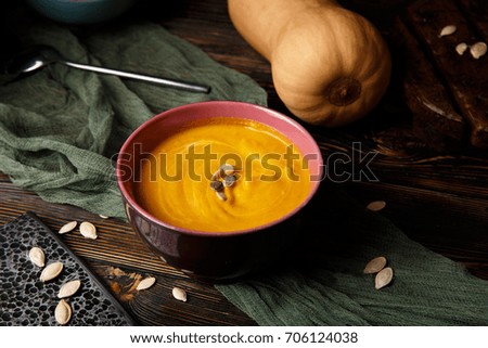 Pumpkin and carrot soup with cream on dark wooden background