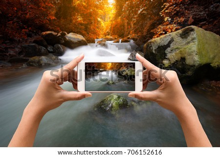 Taking a photos by smartphone of waterfall with flowing river in rain forest in morning. Landscape.