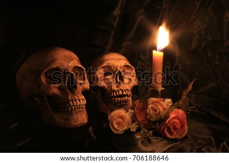 human skulls and pile of withered dry flowers and candle light on black fabric texture on dark background in night time / Still life image and Selective focus