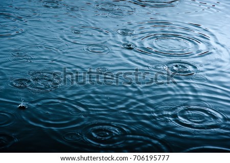 rain drops on the surface of water in a puddle with graduated shade of black shadow and reflection of blue sky Royalty-Free Stock Photo #706195777