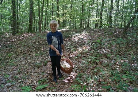 A child, a boy, walks through the forest road in the sunlight with mushroom basket.  big forest mushroom and yellow leaves having fun on a walk on a warm sunny day. Children pick mushrooms.