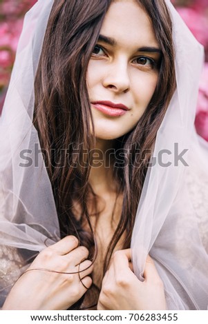 beautiful girl bride brunette closed the veil to the hair, and looks with a smile, happy, close-up, on a background of pink flowers, portrait, close-up