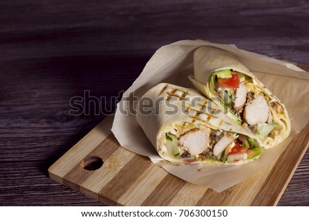 The cut shaverma lies on a wooden board. Shaverm in the section. Shawarma chicken roll in a pita with fresh vegetables and cream sauce on wooden background. Selective focus