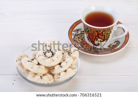 Flower Shaped Persian Sweet Rice Cookies (Naan Berenji) with Poppy Seeds and a paisley design cup and saucer tea on white wooden background 