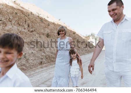 A young beautiful mother with her father and with her son and daughter in white outfits walking along the sandy places. happy family