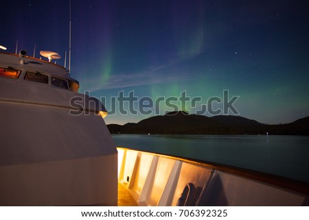 Northern lights over a white cruise ship in Alaska reflecting green off the calm ocean Royalty-Free Stock Photo #706392325