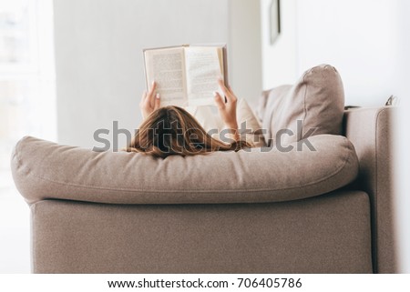 Back view of woman lying on sofa and reading book at home Royalty-Free Stock Photo #706405786