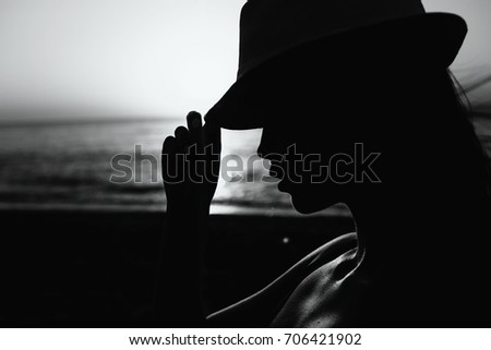 Beautiful girl in a red hat smiling at the summer waterfront. Silhouetted photo in the sunlights at sunset.