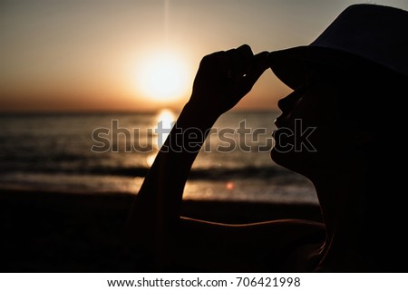 Beautiful girl in a red hat smiling at the summer waterfront. Silhouetted photo in the sunlights at sunset.
