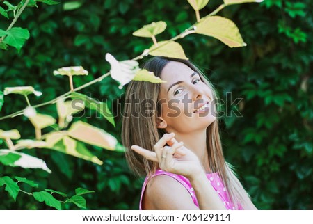 Young beautiful woman has put forefinger to lips as sign of silence, against green summer garden