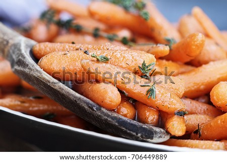 A rustic wooden spoon filled with Honey Glazed Baby carrots for Rosh Hashanah or Thanksgiving Day. Extreme shallow depth of field with selective focus on foreground.