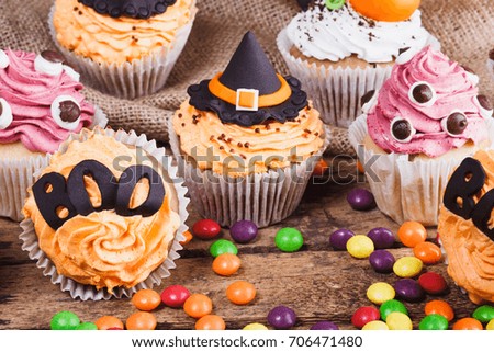 Halloween cupcakes with decorations: tombstone, eyes and orange pumpkins made from confectionery mastic, soft focus background