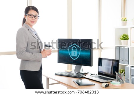attractive happy female businesswoman working on cyber security company and holding coffee cup standing in office face to camera smiling.