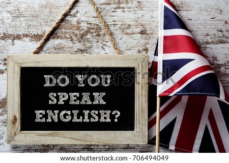 a wooden-framed chalkboard with the question do you speak English? written in it and a flag of the United Kingdom against a rustic wooden background Royalty-Free Stock Photo #706494049
