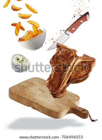 Grilled T-bone steak floating ingredients concept with a chopping board, healthy lean steak, French fries and tzatziki in bowls, spices and a sharp knife isolated on white Royalty-Free Stock Photo #706496053