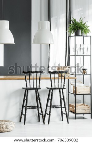 Plant on black shelf next to black bar stools at countertop with white lamps in rustic dining room