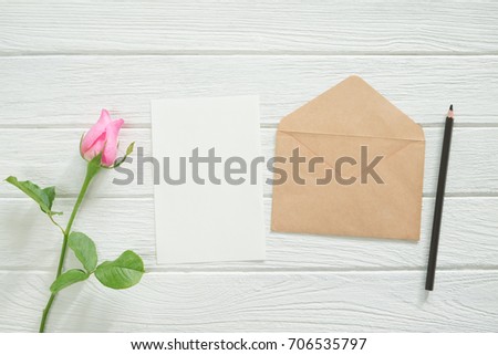 Blank paper with rose flower and brown envelope on table.top view