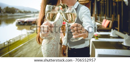Husband and wife kiss together. There is hands holding glasses of wine in the foreground. Focus at hands holding glasses of wine. Shallow depth of field.