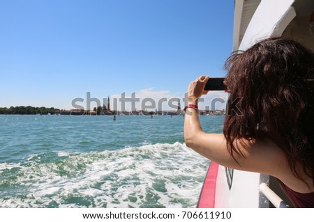 young woman with long brown hair takes picture of Venice in Italy by boat in the sea