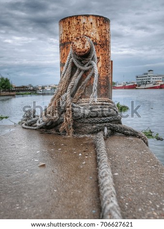 Old rusted mooring bollard with knotted nautical ropes. mooring ropes