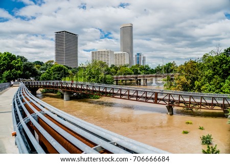 High and fast water rising in Bayou River from Rosemont pedestrian bridge with near town Houston in background, cloud blue sky. Heavy rains from Harvey Tropical Hurricane storm caused many flood areas