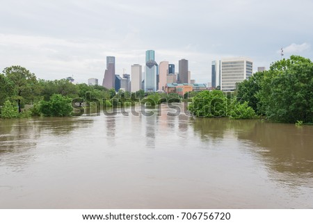 High and fast water rising in Bayou River along Allen Parkway and Memorial Drive with downtown Houston in background under storm cloud sky. Heavy rains from tropical storm caused many flooded areas