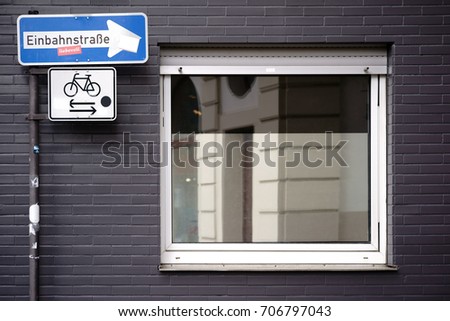 A vertically standing one-way street sign at the corner of a clipped residential building with a window / One-way street sign at home corner